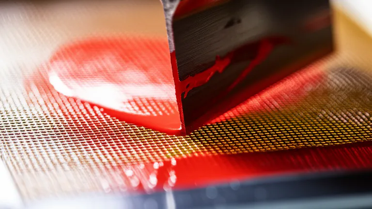 Detalle macro de malla serigráfica con tinta plastisol siendo aplicada sobre tejido